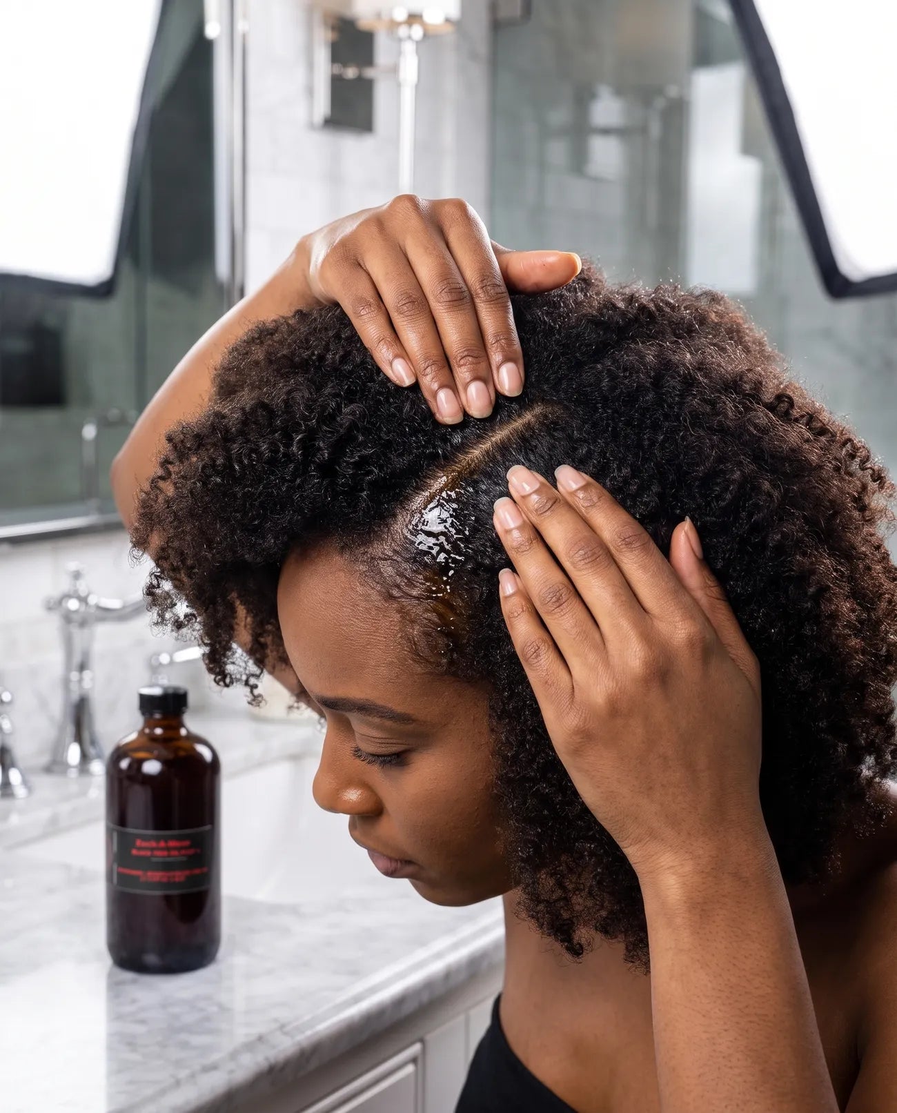 Black seed oil being massaged into the scalp along a part between locs